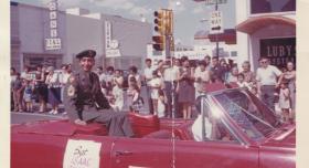 Color historical photo of Isaac Camacho in a red convertible during a parade