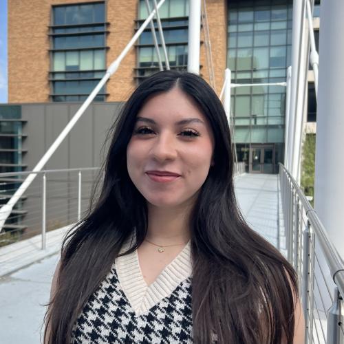 Headshot of Yvette Garcia. She wears a houndstooth shirt and is at the Moody College of Communication bridge at UT Austin.